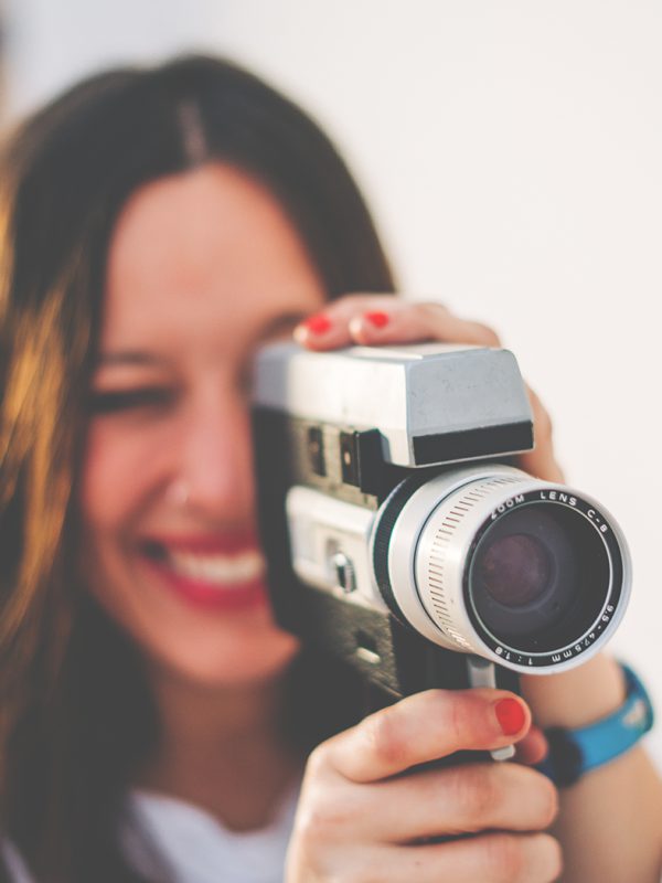 young smiling woman with red lips using a retro video camera isolated on a white background